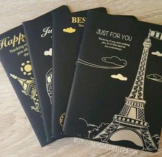 three black passport covers with the eiffel tower in gold foil on them, sitting on a wooden surface