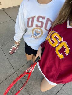 two girls are holding tennis rackets on the sidewalk outside their school's building