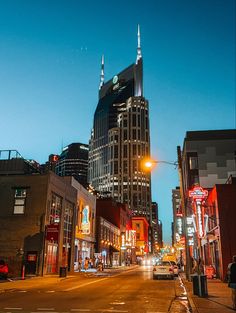 a city street at night with tall buildings in the background