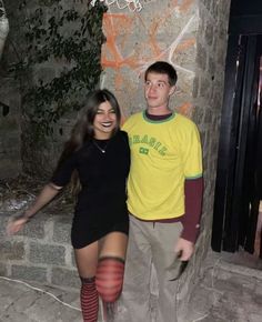 a man and woman standing next to each other in front of a wall with graffiti on it