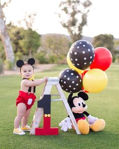 a baby standing on a ladder next to mickey mouse balloons