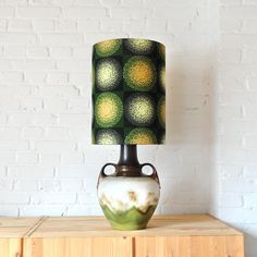 a green and yellow lamp sitting on top of a wooden table next to a white brick wall