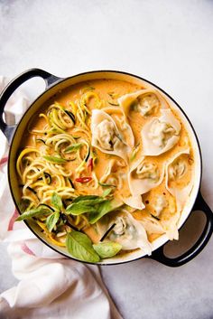 a pot filled with pasta and vegetables on top of a white tablecloth next to a napkin