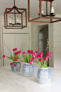 three blue and white vases with pink flowers in them on a kitchen countertop