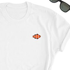 Fish Clownfish Shirt, Clownfish Lover T-shirt, Fish Lover Shirt, Ocean Lover Simple T-shirt, Clownfish Lover Gift, Fish Unisex T-Shirt, Fish Take this one by your side everywhere. Friends will love it! This t-shirt feels soft and lightweight, with the right amount of stretch. It's comfortable and flattering for both men and women. * 100% cotton (heather colors contain polyester) * Fabric weight: 5 oz * Shoulder-to-shoulder taping * Side-seamed Time for Delivery: * Processing & production tim Fish T Shirt Design, Summer Crew Neck T-shirt With Fish Print, White Fish Print Shirt For Summer, Casual Crew Neck T-shirt With Fish Print, Casual White Fish Print Top, White Cotton T-shirt With Fish Print, White Casual Shirt With Fish Print, Graphic Tee T-shirt With Fish Print, Graphic Fish Print Short Sleeve T-shirt