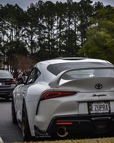 the rear end of a white toyota sports car driving down a street with trees in the background