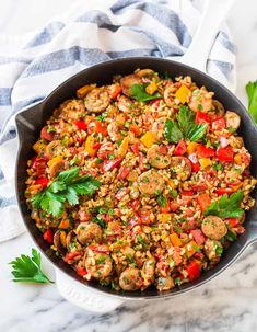 a skillet filled with rice and vegetables on top of a marble counter next to parsley