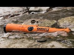 an orange blow dryer sitting on top of a rock next to some water and coins