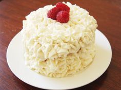 a cake with white frosting and raspberries on top sitting on a plate