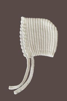 a white knitted hat with tassels on the top and side, against a brown background