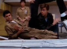 a group of people standing around a man laying on top of a bed in a hospital