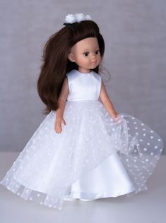 the doll is wearing a white dress with polka dots on it and she has long brown hair