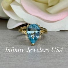 a blue topazte ring sitting next to a white rose with the words infinity jewelers usa on it