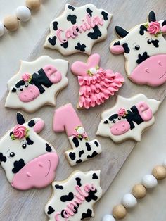 decorated cookies are arranged on a table with white and pink frosting, including cow