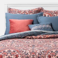 a bed with blue and red comforters, pillows and blankets on top of it