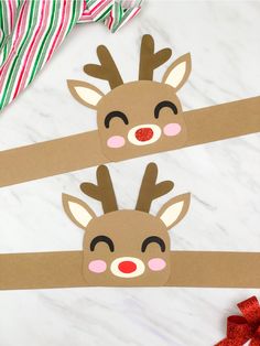 two reindeer head cut out from cardboard on top of a white marble table with red and green striped ribbon