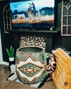 a person holding a coffee mug in front of a television with a cowboy scene on it