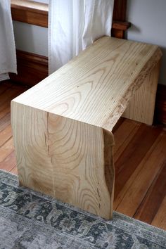 a wooden bench sitting on top of a hard wood floor next to a white curtain