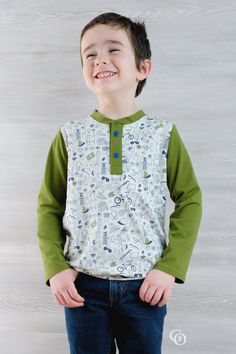 a young boy standing in front of a wooden wall wearing a green and white shirt