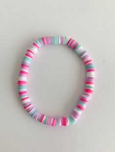 a pink, blue and green striped bracelet on a white surface with a black bead