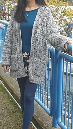 a woman standing next to a blue fence with her hand on her hip and looking at the camera