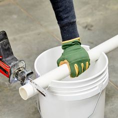 a person in green gloves is holding a white bucket with a drill and some tools