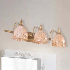 three light bathroom fixture with pink glass shades on the wall and mirror in the background