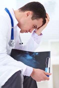 a male doctor is holding his head in his hands and looking at an x - ray