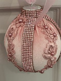 a pink ornament hanging from a door with ribbon and beading on it