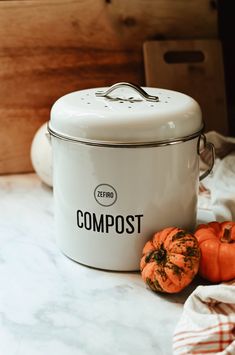 a white canister sitting on top of a counter next to two small pumpkins