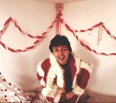 a man in a red and white fur coat standing next to a decorated christmas tree