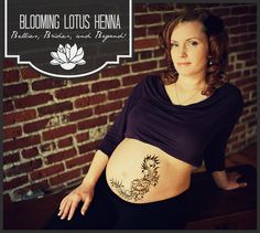 a pregnant woman sitting on a bench with her belly covered by tattoos and flowers in front of a brick wall