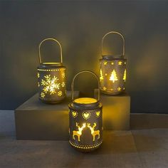 three lit up christmas lanterns with deer and snowflakes on them, sitting next to each other