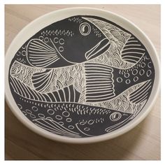 a black and white plate with fish on it sitting on a wooden table next to a cup