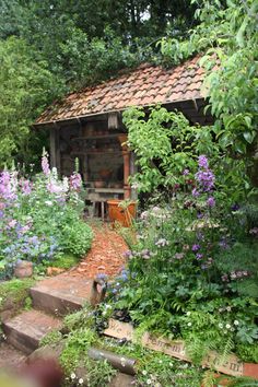 an old shed is surrounded by flowers and greenery in the garden with steps leading up to it