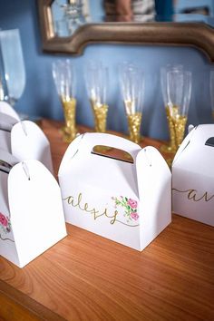 three white boxes with floral designs on them sitting on a table next to champagne glasses