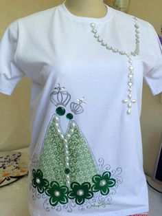 a white t - shirt with a green dress and pearls on the front, sitting on a mannequin