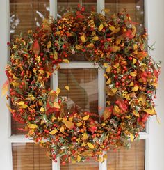 a wreath is hanging on the window sill with autumn leaves and berries around it