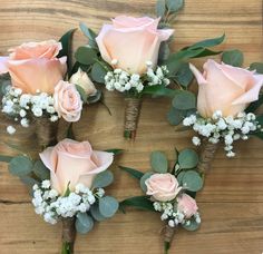 six pink roses and baby's breath are arranged on a wooden table with greenery