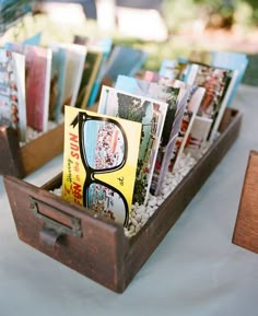 a wooden box filled with lots of books on top of a white table covered in photos