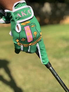 a person wearing green golf gloves and holding a golf club in their hand with the word aka on it