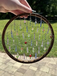 a person holding up a glass bead dream catcher in front of a grassy area