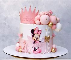 a pink and white cake with a minnie mouse design on the top is surrounded by balloons