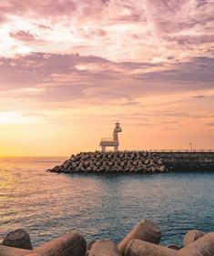 a light house sitting on top of a pier next to the ocean in front of a sunset