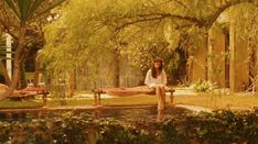 a woman sitting on top of a wooden bench under a tree next to a lush green park