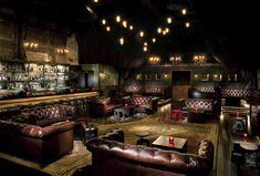 a dimly lit bar with leather couches and tables in the center, lights hanging from the ceiling