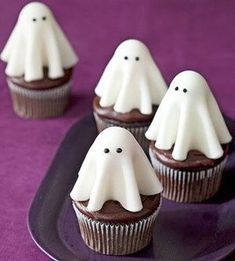 three cupcakes with white frosting and ghost faces on them sitting on a purple plate