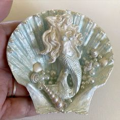 there is a small shell with a mermaid on it and pearls in the shells around it