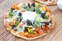 two small pizzas with different toppings sitting on top of a wooden table next to a bowl