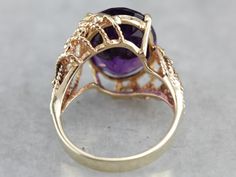 "A deep eggplant purple amethyst glitters with light and flash at the center of this asymmetrical, Mod style cocktail ring! Light and airy for all of its substantial size, this vintage piece is sure to make an impression! Metal: 10K Yellow Gold Gem: Amethyst 7.33 Carats Gem Measurements: 15.8 x 11.7 mm, Oval Ring Size: 6.75 Marks: \"10K\" Stamped on the inside band SKU #: A92FJV Each piece has been identified and graded by a Graduate Gemologist who has been certified by the Gemological Institute Luxury Antique Purple Amethyst Ring, Vintage Amethyst Rings With Polished Finish, Luxury Vintage Amethyst Ring With Polished Finish, Luxury Yellow Gold Amethyst Ring Collectible, Vintage Amethyst Jewelry With Polished Finish, Mod Style, Expensive Jewelry Luxury, Eggplant Purple, Jewelry Luxury